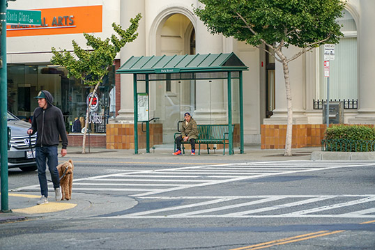 Image of a bus shelter with a person sitting on a bench waiting for the bus.
