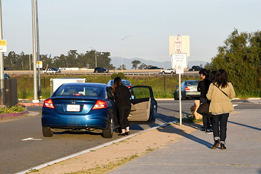 Image of one person getting into car just off of the curb and three people on the curb looking at the car.