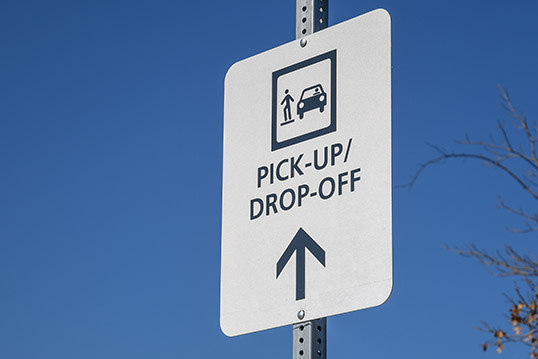 Image of a sign reading pick-up/drop off and an icon of a person on a curb next to a car.