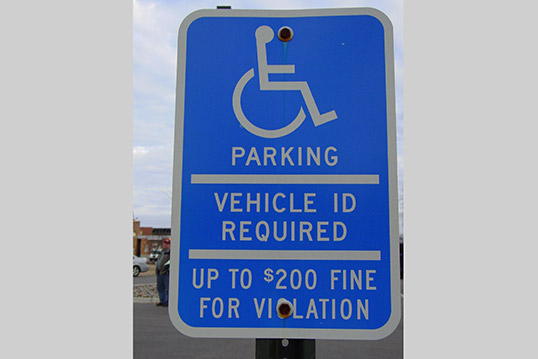 Image of a bright blue sign with an icon of a person in a wheelchair and the words Parking, Vehicle ID Required, Up to $200 fine for violation