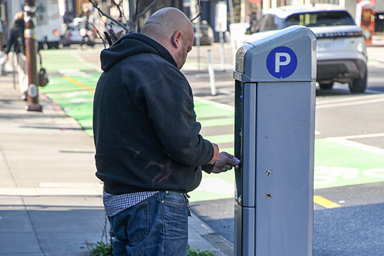 Image of a person paying for parking at a curb-side podium with a large P icon on the side