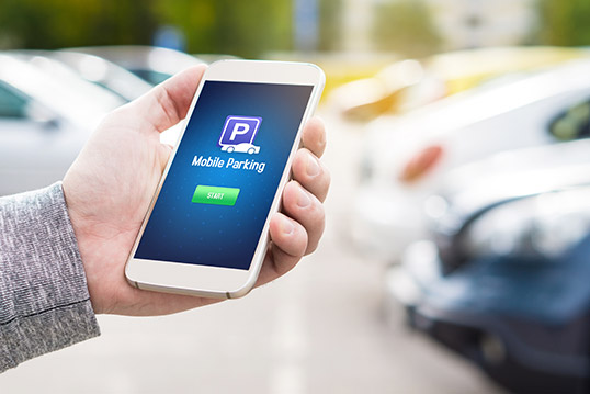 Image of a phone showing landing page for a mobile parking app, in someone's hand with blurry cars in the background