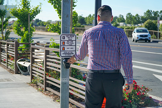 Image of a person pressing the walk button to cross street next to clearly marked signal crossing sign.