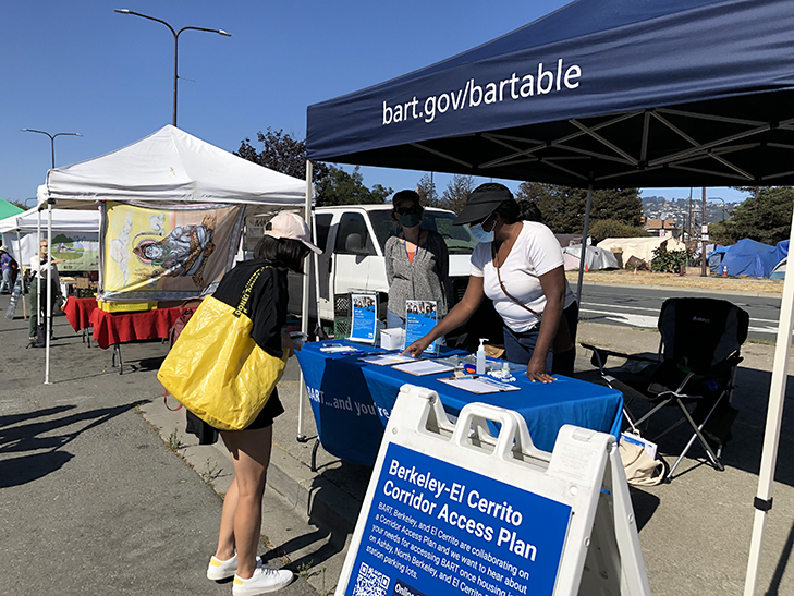 BART staff at a booth at a farmers market talking with a person about the Berkeley-El Cerrito Corridor Access Plan. This is one of the ways BART shared information and learned from BART riders and nearby residents in 2021.
