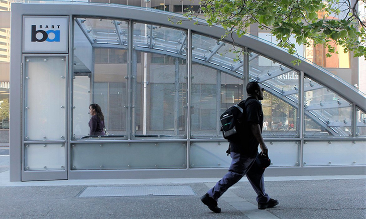 A person walking in front of a BART station entrance, demonstrating one of the many different ways people travel to and from BART stations. This is called station access.
