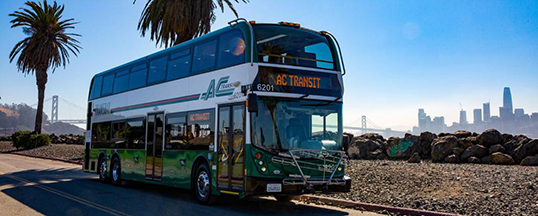 A double decker Transbay bus with the Bay Bridge and Downtown San Francisco in the background.