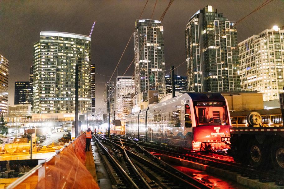 Un tren ligero Link está siendo empujado a lo largo de las vías justo al este de la estación Bellevue Downtown por la noche