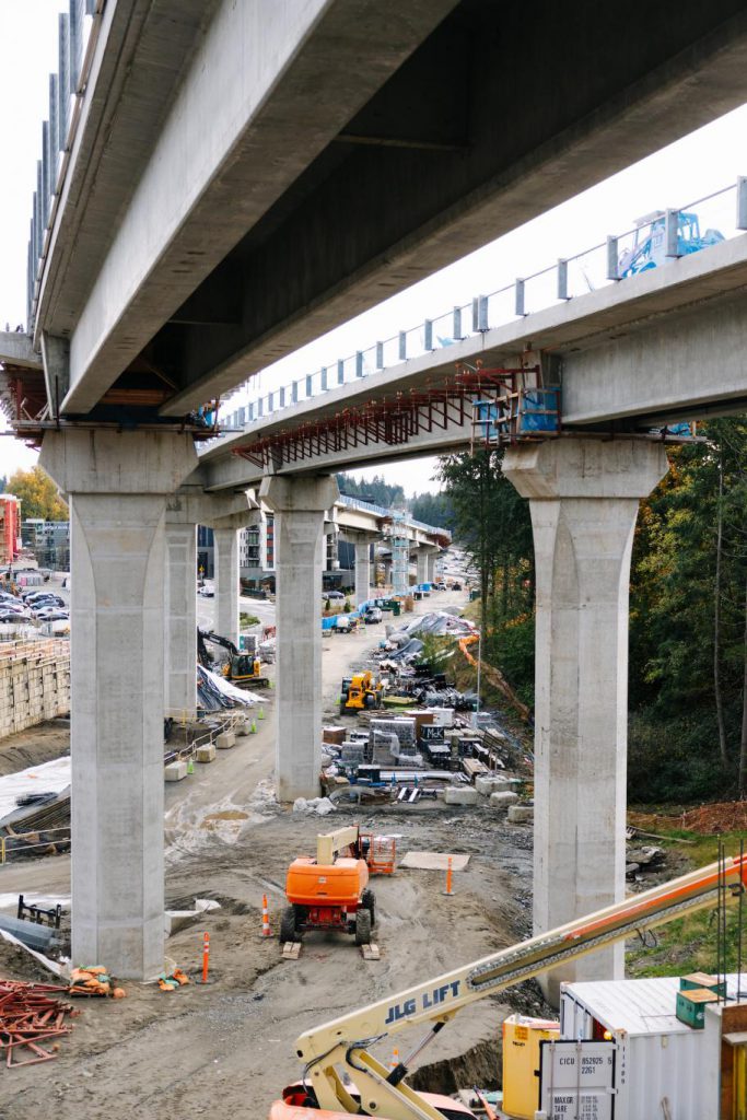 Установленные мостовые подпорки для возвышенных путей наземного метрополитена; строительное оборудование разложено на земле неподалеку. 