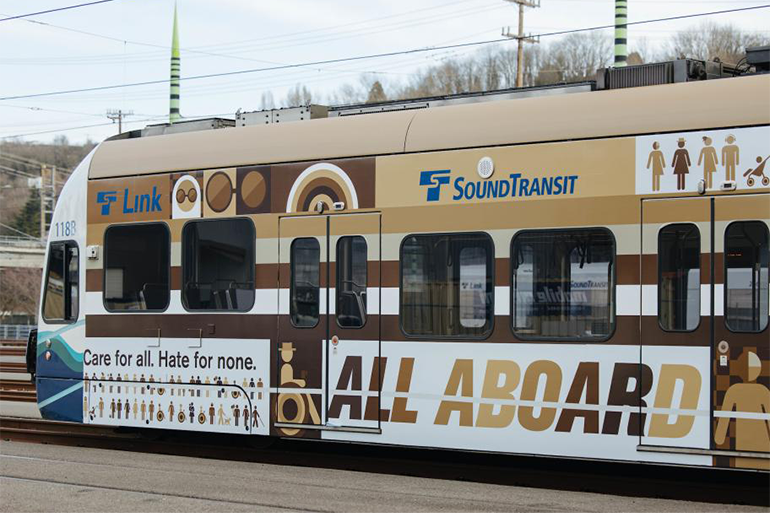 Link 轻轨列车装饰有'All Aboard'活动标语，其中包括不同肤色的字母和残疾乘客的图形。 