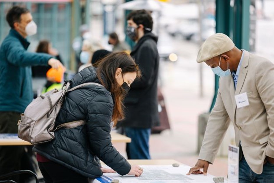 Photo showing community members submitting comments at a station area tabling event. Two commenters, both wearing masks during the pandemic, look at a map of station and route alternatives. One community member is leaving a hand-written comment for the project team to consider. The Everett Link Extension will host both in-person and virtual engagement opportunities.