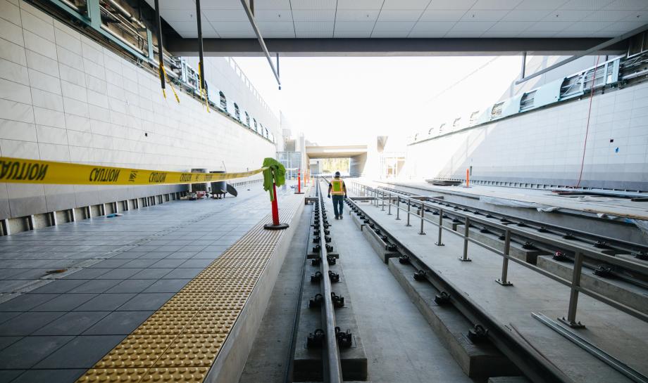Photo showing a construction worker walking along rail lines built for a future Link light rail station. The station is located below ground-level, but is an open-air station, meaning the station is not located fully underground in a tunnel. This photo shows an example of what a station could look like at Evergreen for the open station alternative.