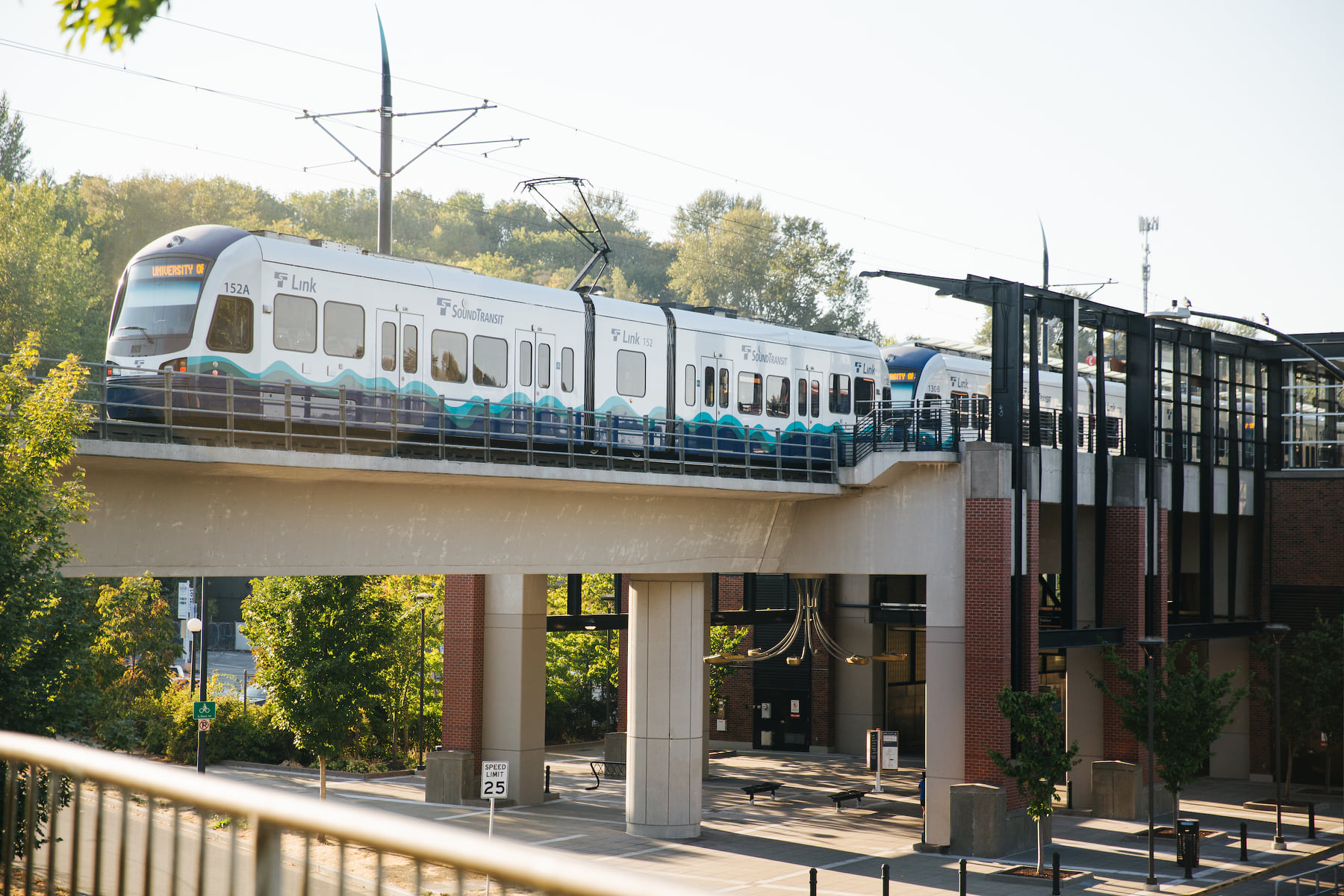 Photo showing a Link light rail train leaving an existing light rail station. The station is elevated from the ground level, and the rail line runs above street level. The photo shows an example of what an elevated station, like the one that will be built at Mariner, could look like.