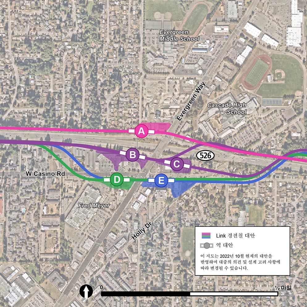 이 지도는 5개의 Evergreen Link 스테이션 대안과 각각의 풋프린트를 보여줍니다. 역 대안 A는 A라고 표시된 분홍색 원으로 표시되어 있습니다. 역은 Evergreen Way와 SR-526 교차로의 북서쪽 모퉁이에 있습니다. 희미한 분홍색 모양으로 상징되는 역의 풋프린트는 Beverly Lane과 Evergreen Way 사이에 있습니다. 역의 경전철 대안은 분홍색 선으로 상징되며 SR-526 바로 북쪽에 위치하며 평행을 이룹니다. 역 대안 B는 B라고 표시된 자주색 원으로 표시됩니다. 역은 SR-526과 Evergreen Way 교차로의 남서쪽에 있습니다. 두 개의 희미한 보라색 직사각형으로 상징되는 역의 발자국은 Casino Road를 향해 남쪽으로 뻗어 있습니다. 자주색 선으로 상징되는 역 대안의 경전철 트랙은 서쪽에서 동쪽으로 이어지고 Evergreen Way를 가로지른 다음 SR-526 동쪽과 평행을 이루기 전에 북쪽으로 SR-526을 가로지릅니다. 역 대안 B는 B라고 표시된 자주색 원으로 표시됩니다. 역은 SR-526과 Evergreen Way 교차로의 남서쪽에 있습니다. 두 개의 희미한 보라색 직사각형으로 상징되는 역의 풋프린트는  Casino Road를 향해 남쪽으로 뻗어 있습니다. 자주색 선으로 상징되는 역 대안의 경전철 트랙은 SR-526과 평행하게 서쪽에서 동쪽으로 달린 다음 Evergreen Way를 건너 SR-526 동쪽으로 평행하게 달리기 전에 SR-526을 북쪽으로 교차합니다. 역 대안 C는 C로 표시된 자주색 원으로 표시됩니다. 역은 Evergreen Way와 SR-526 교차로의 남서쪽에 있습니다. 역의 풋프린트는 작고 희미한 자주색 사각형으로 상징됩니다. 보라색 선으로 상징되는 역 대안의 경전철 트랙은 SR-526과 평행하게 서쪽에서 동쪽으로 달리고 역 대안 C에 진입하기 전에 Evergreen Way를 건너 동쪽으로 계속 진행하여 SR-526을 통해 북쪽으로 건너갑니다. 역 대안 D는 D라고 표시된 녹색 원으로 표시됩니다. 역은 Casino Road와 Evergreen Way 교차로의 남서쪽에 있습니다. 희미한 녹색 반원으로 상징되는 역의 발자국은 Fred Meyer를 향해 남쪽으로 확장됩니다. 녹색 선으로 상징되는 역 대안의 경전철 트랙은 SR-526과 평행하게 서쪽에서 동쪽으로 달리다가 W Casino Road에서 남쪽으로 휘어져 역에 진입하고 Evergreen Way를 건너 SR-526 위로 다시 북쪽으로 휘어집니다. 역 대안 E는 E라고 표시된 파란색 원으로 표시됩니다. 역은 Casino Road와 Evergreen Way 교차로의 남동쪽에 있습니다. 희미한 파란색 삼각형으로 상징되는 역의 풋프린트는 Holly Drive를 향해 남동쪽으로 확장됩니다. 파란색 선으로 상징되는 역 대안의 경전철 트랙은 SR-526과 평행하게 서쪽에서 동쪽으로 달리다가 W Casino Road를 지나 남쪽으로 휘어지고 Evergreen Way를 건너 역에 진입한 다음 SR-526 위로 다시 북쪽으로 휘어집니다..